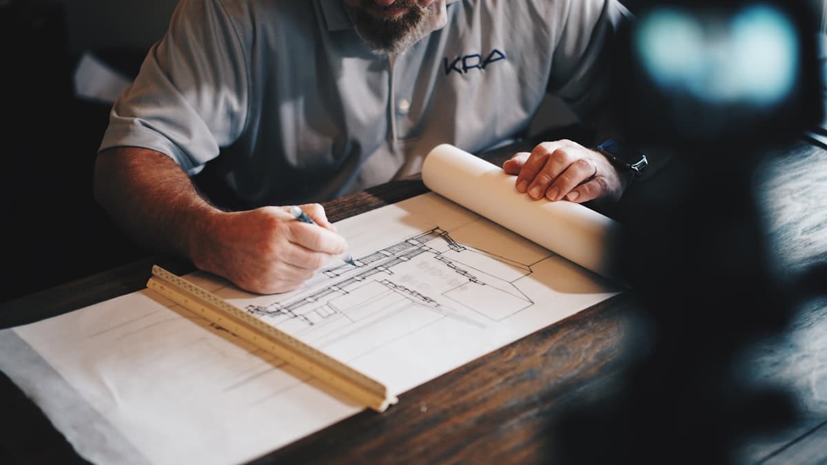 Hands drafting a technical drawing with a scale ruler